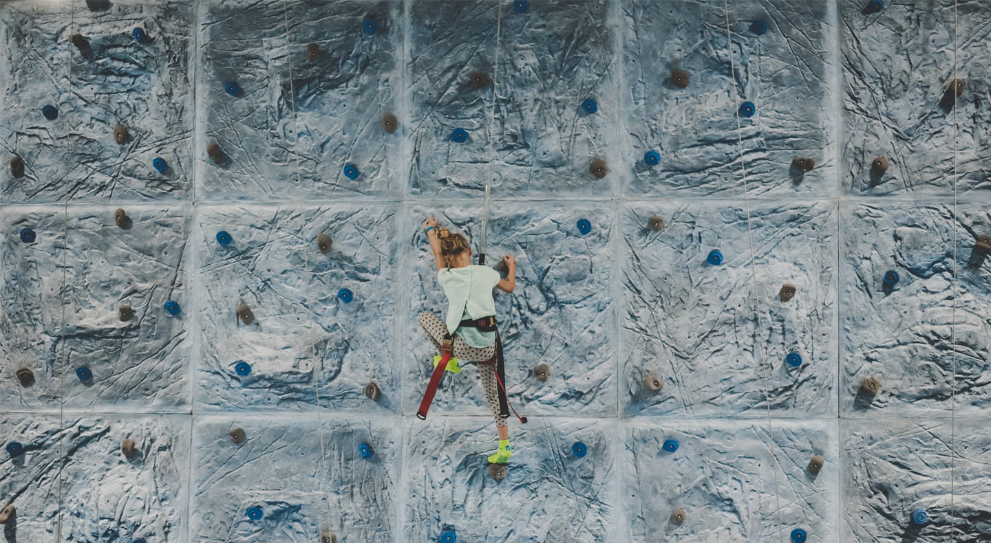 young women climbing up a climbing wall